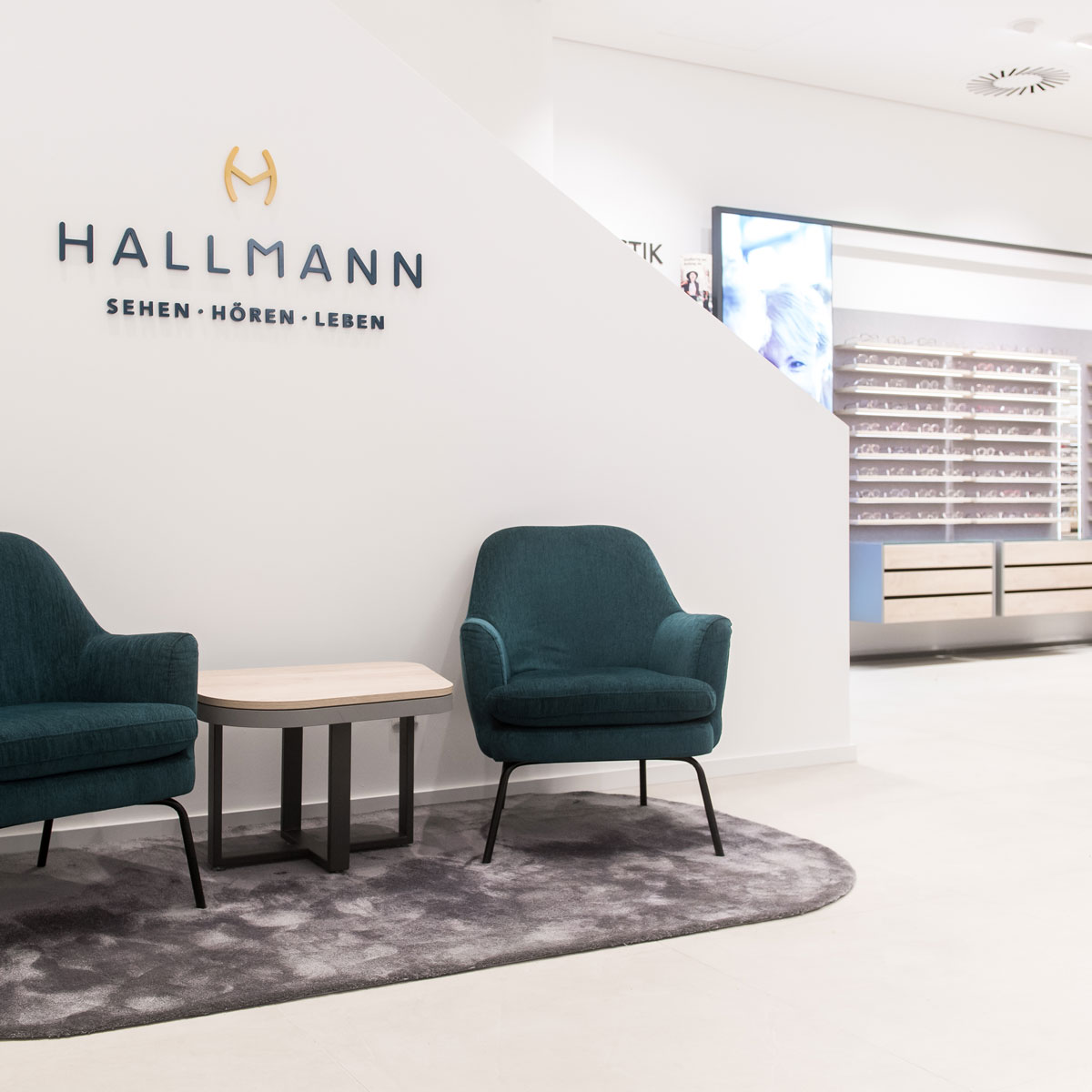 Wartebereich im Optikergeschäft mit Sesseln und Markenlogo an der Wand